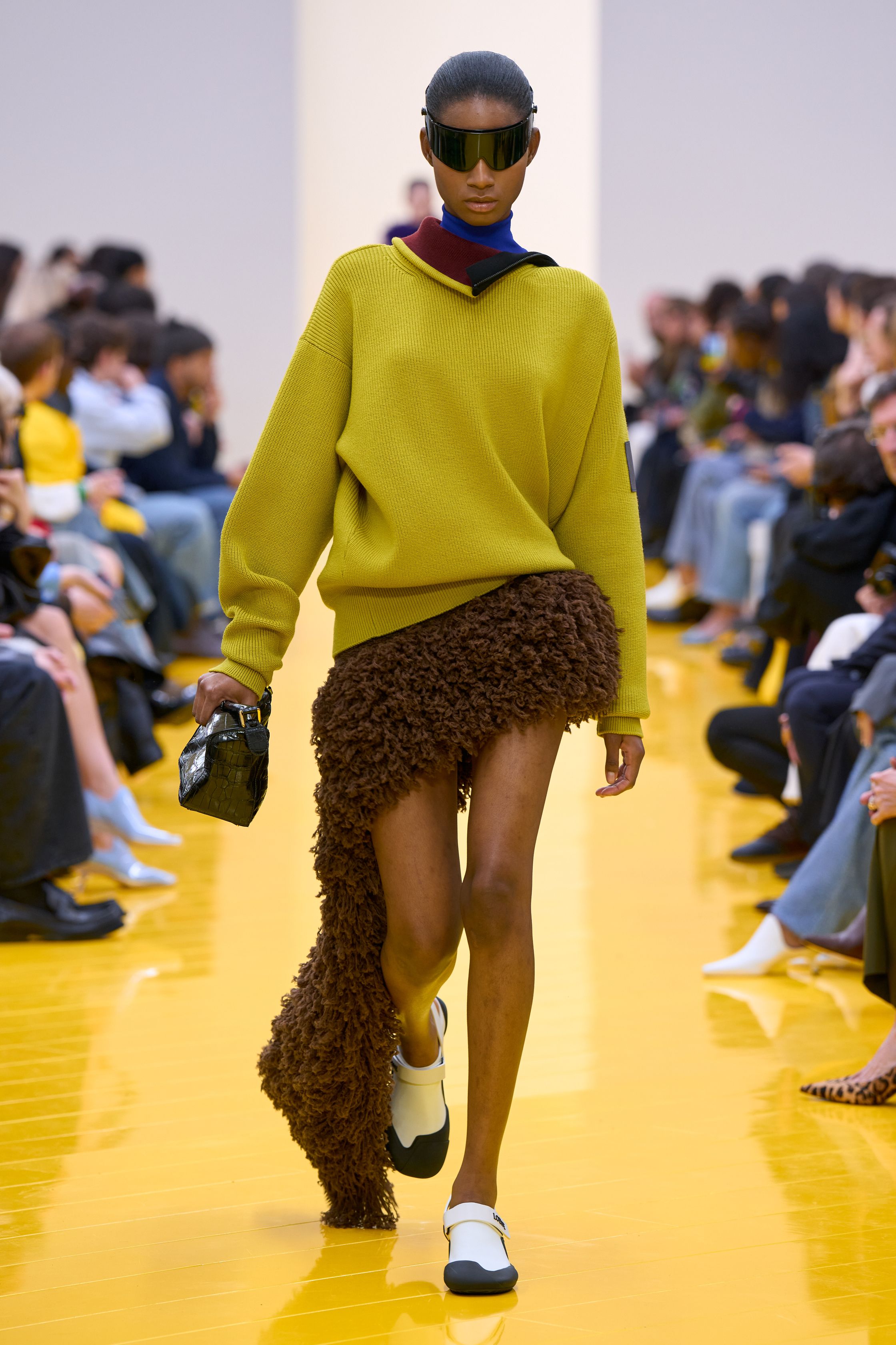 Jonathan Anderson 为 Loewe 带来一场充满艺术实验的秀：黄色地面与鲜明色彩形成强烈视觉舞台，极简廓形针织、雕塑化皮革外套、夸张毛绒结构和实验比例裙装共同构建一种“可穿戴雕塑”。从鲜黄、亮蓝到浓郁棕色毛绒，材质对比成为本季核心语言，既有幽默感也带有博物馆式艺术气质-顽石频道趋势研究